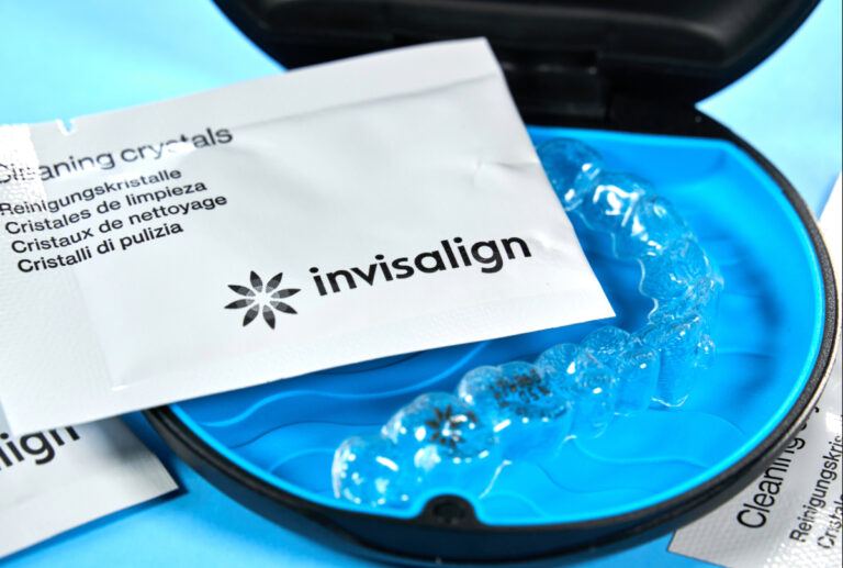 Clear aligner in an open blue case beside Invisalign cleaning crystal packets